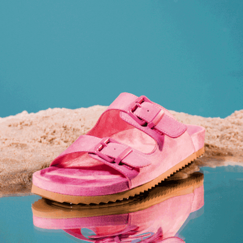 Pink slipper with buckles standing on water and sand