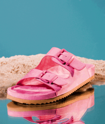 Pink slipper with buckles standing on water and sand