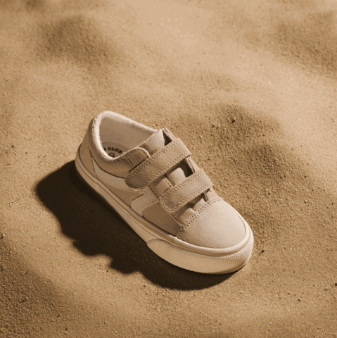 Beiger Kinderschuh aus Canvas steht im Sand