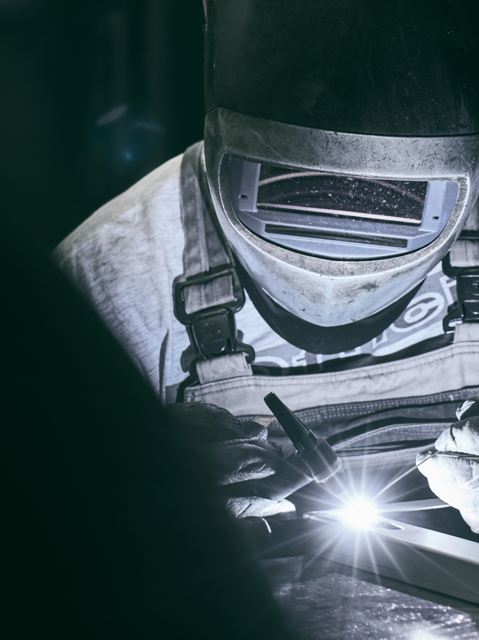 A welder wearing mask and gloves welding on a metal plate