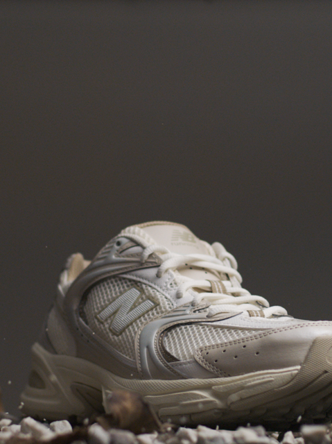 White and beige New Balance sneaker standing on stones and brown leafes