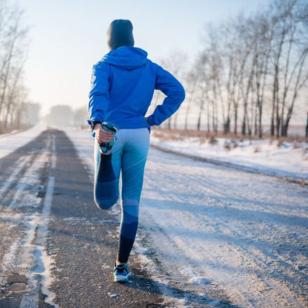 Runner in blue sportswear standing in the snowy street and stretching out
