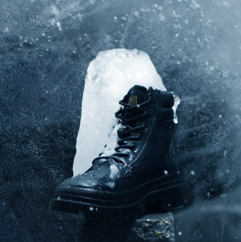 A black winter boot is standing on a rock half frozen into a big icecube