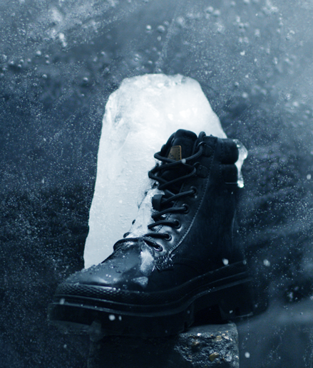 A black winter boot is standing on a rock half frozen into a big icecube