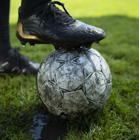 Close-up of a black football shoe placed on top of a white football