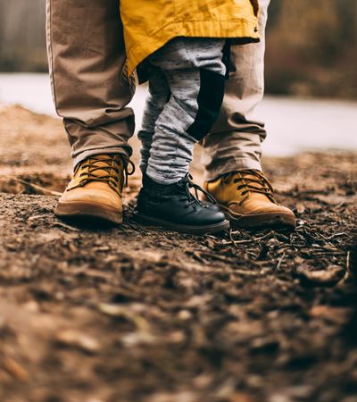 Father in brown leather boots and child in black leather boots standing togehter in the woods