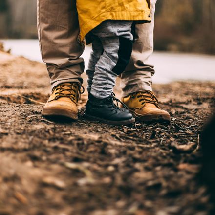 Father in brown leather boots and child in black leather boots standing togehter in the woods