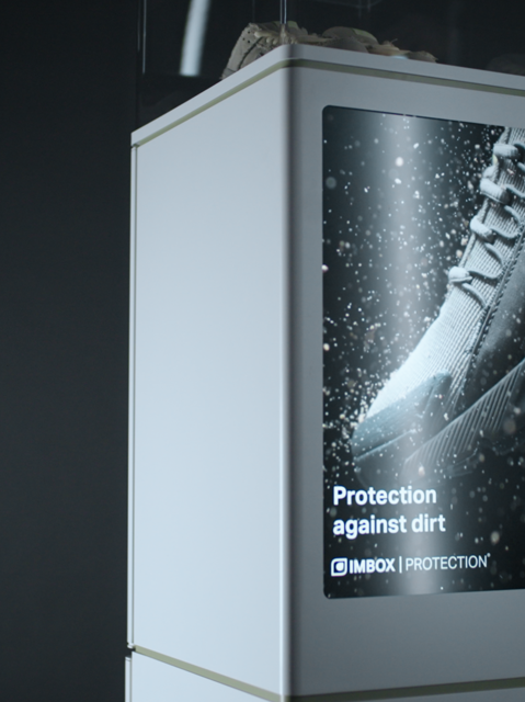 White IMBOX Flagship with promotional video playing with white sneaker on top inside the transparent box