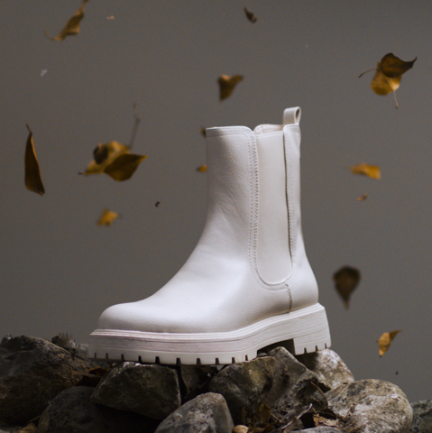 IMBOXed white chelsea boot standing on top of stones sorounded by leaves falling down