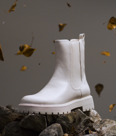 IMBOXed white chelsea boot standing on top of stones sorounded by leaves falling down