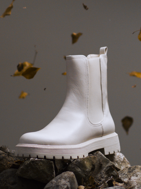 IMBOXed white chelsea boot standing on top of stones sorounded by leaves falling down