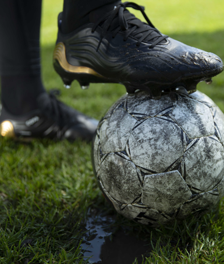 Close-up of a black football shoe placed on top of a white football