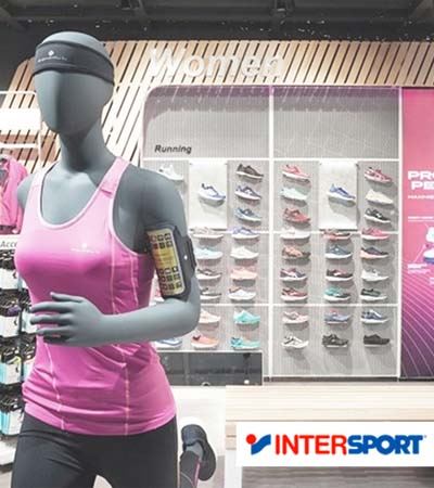 View of Intersport store with running mannequin in front and shoe shelves and shoes in the background with red and blue Intersport logo